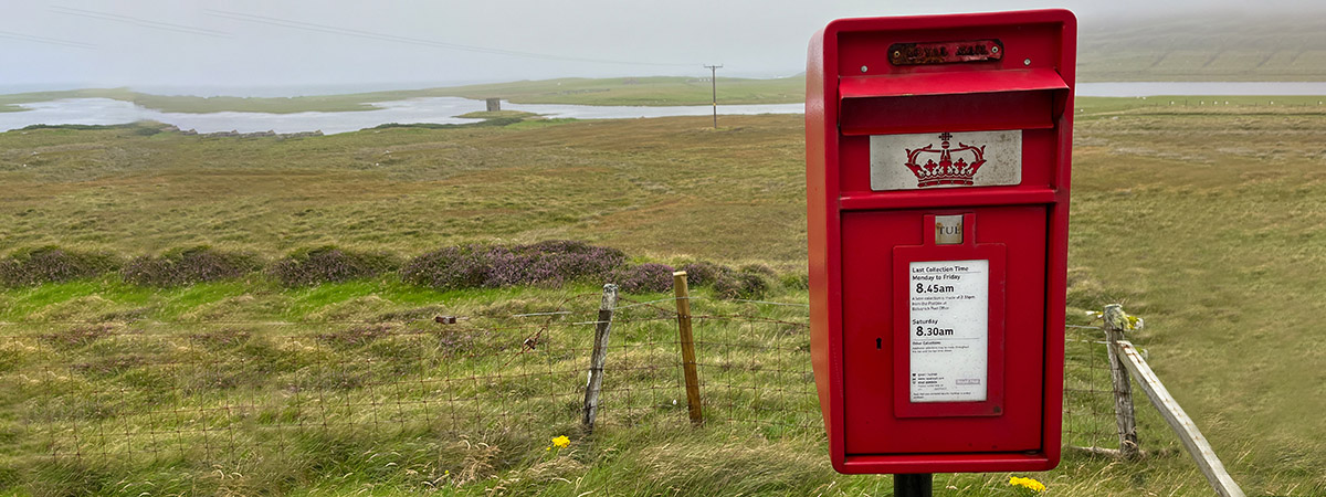 Traditioneller roter Briefkasten vor nebliger Naturkulisse.