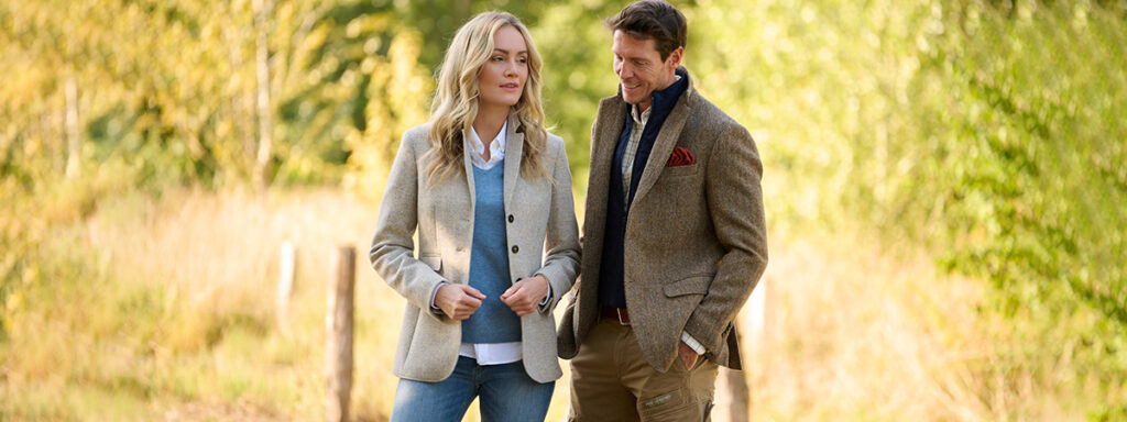 Couple in front of a country lane, woman in cream Harris Tweed blazer and man in Harris Tweed jacket with vest insert